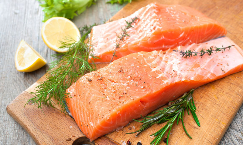 Filés de salmão grelhados, sobre uma tábua de madeira, com decoração de limão e alecrim.